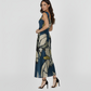 One-shoulder evening dress with a deep midnight blue base and contrasting neutral-toned floral accents. The back design features a clean, high-cut finish on one side, showcasing the sophisticated drape of the fabric for special occasions.