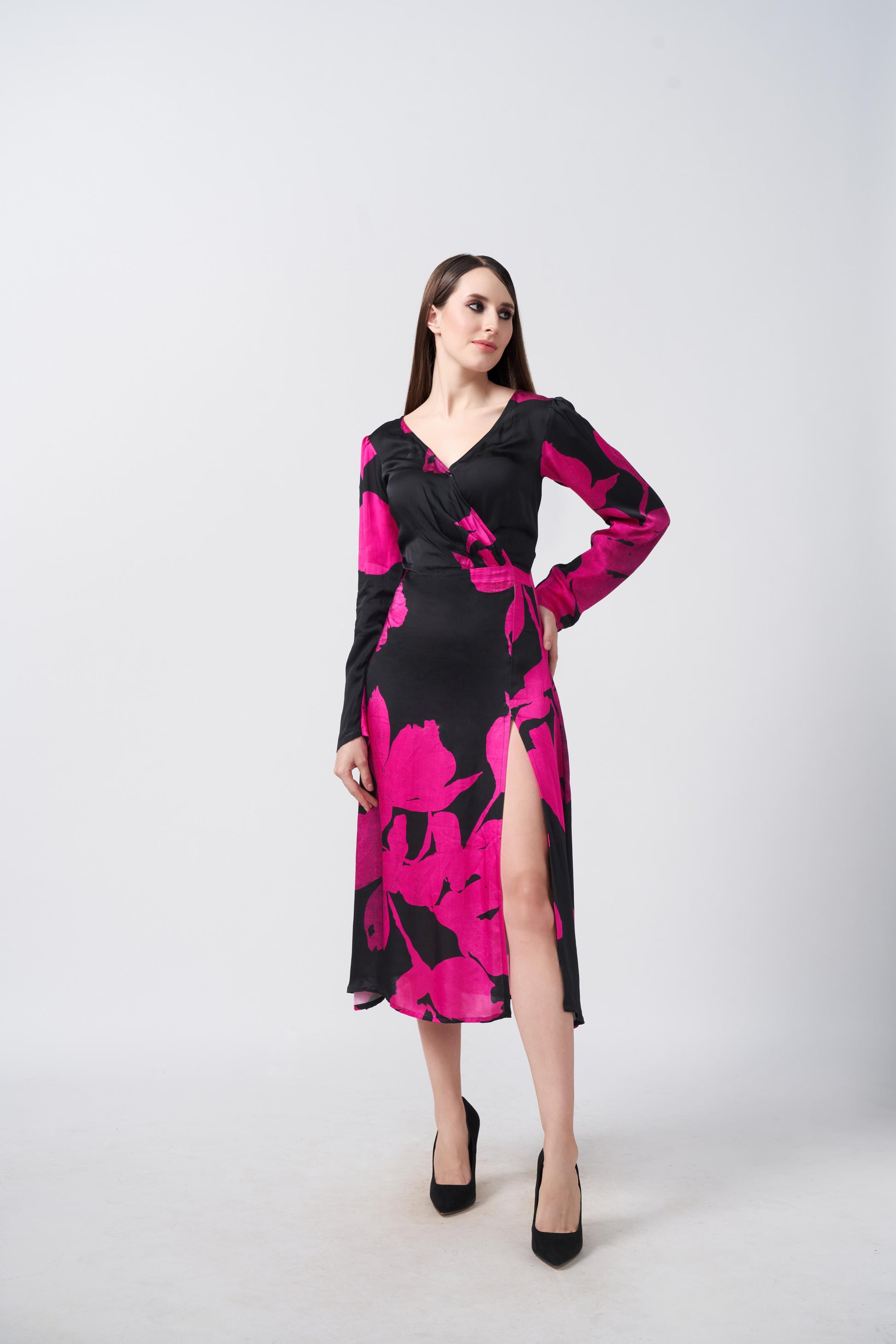 Model posing with hands on waist in silk midi dress with long sleeves and floral print in black and pink tones.