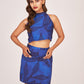 Model poses with both hands on waist in blue floral halter co-ord set, showing the fitted top and playful printed skirt.