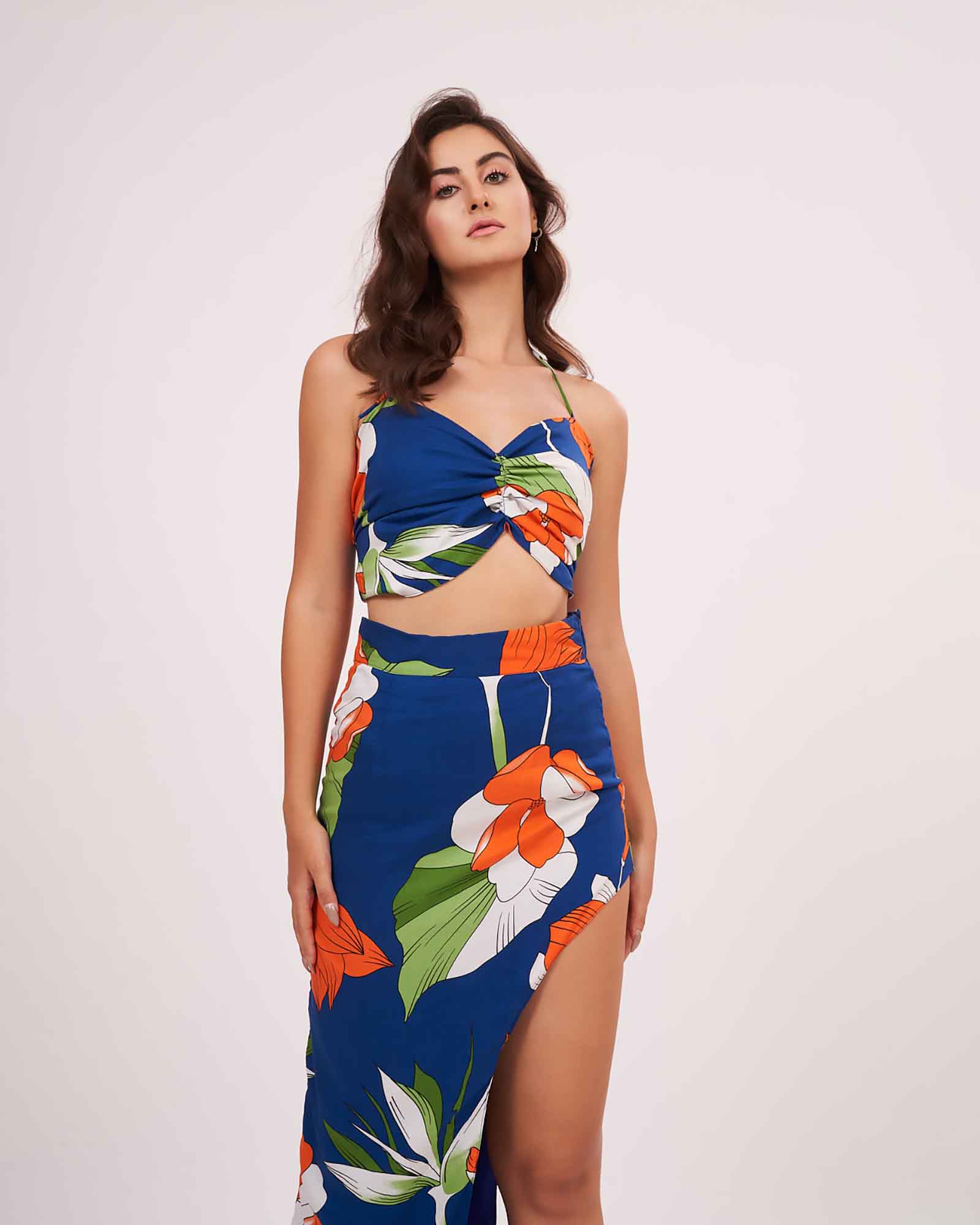 Front-facing pose with relaxed arms, showing the floral print detail and ruched bodice design of the blue halter neck top.