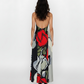Back view of a model wearing a floor-length, backless halter maxi dress. The fabric features a bold, large-scale abstract floral print with prominent red roses and grey-toned petals.