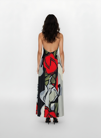 Back view of a model wearing a floor-length, backless halter maxi dress. The fabric features a bold, large-scale abstract floral print with prominent red roses and grey-toned petals.
