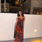Full-length shot of a woman in a red and black floral chiffon dress with spaghetti straps, posing with hands on the side