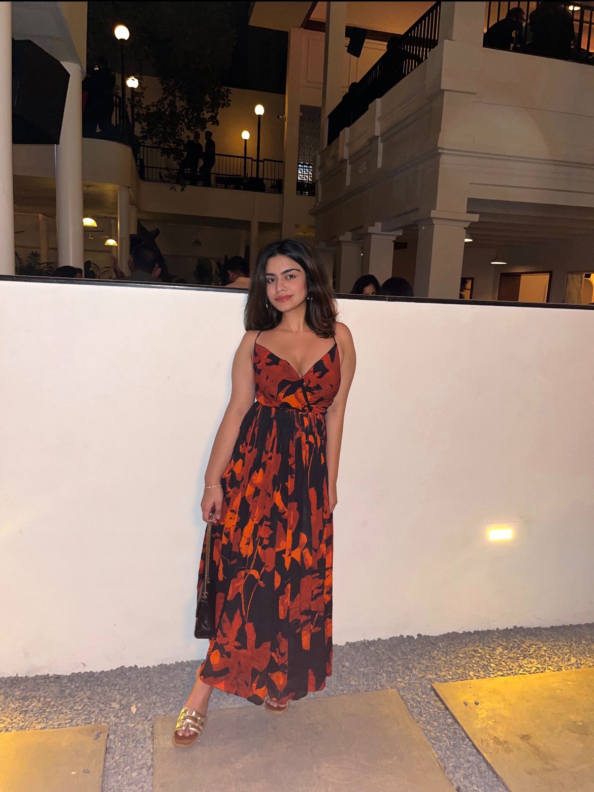 Full-length shot of a woman in a red and black floral chiffon dress with spaghetti straps, posing with hands on the side