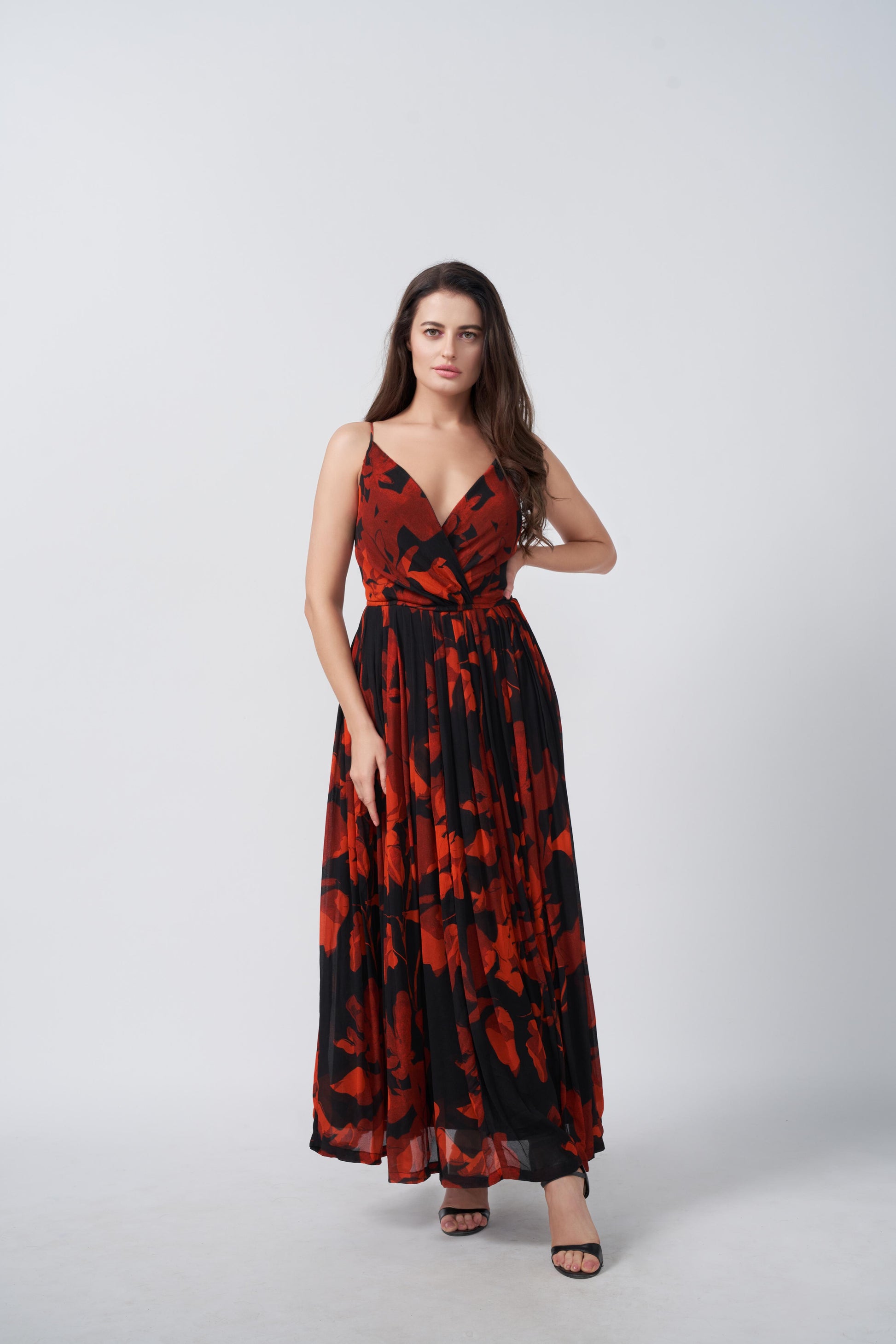 Woman wearing a red and black floral chiffon dress with spaghetti straps, with one hand on waist
