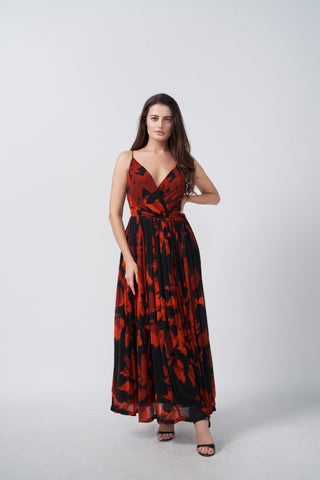 Floor-length maxi dress defined by a wrap-style V-neckline and a cinched waist that transitions into a sweeping pleated skirt. The striking red and black botanical pattern makes a bold statement for formal evening events.