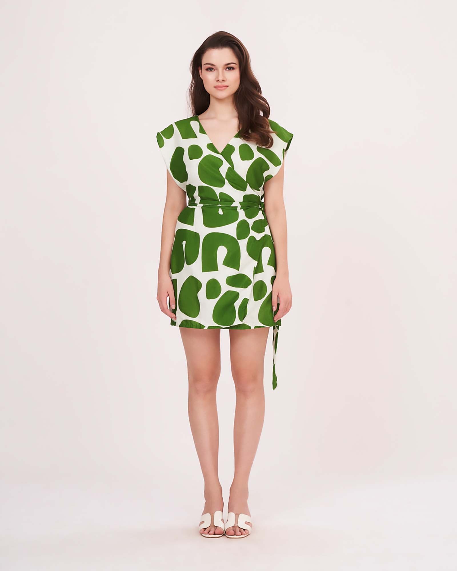 Full front view of model wearing sleeveless green wrap dress with belt tie-up and abstract pattern.