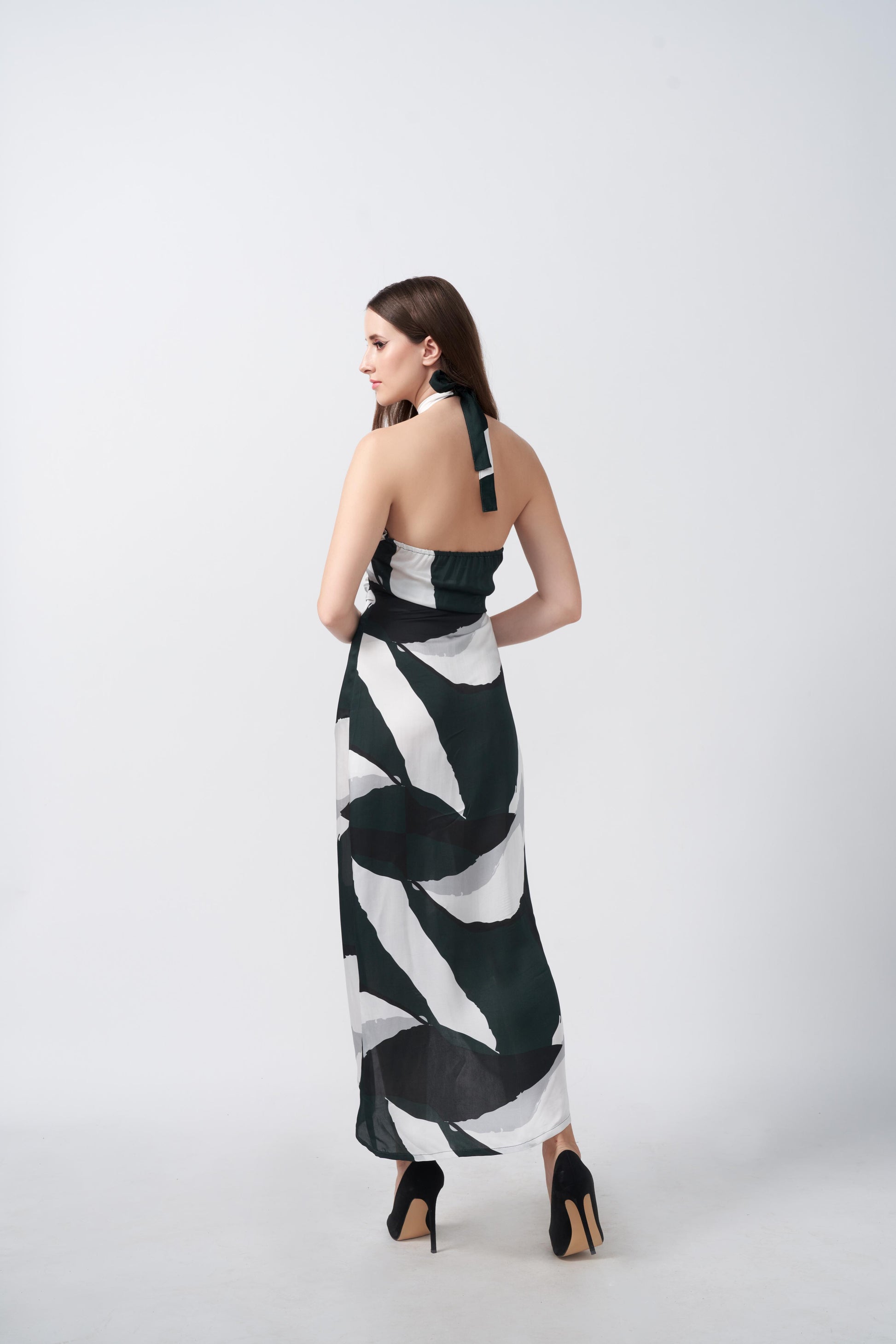 Back view of the model in green, black, and white satin dress with tie-back halter neckline and asymmetrical hemline.