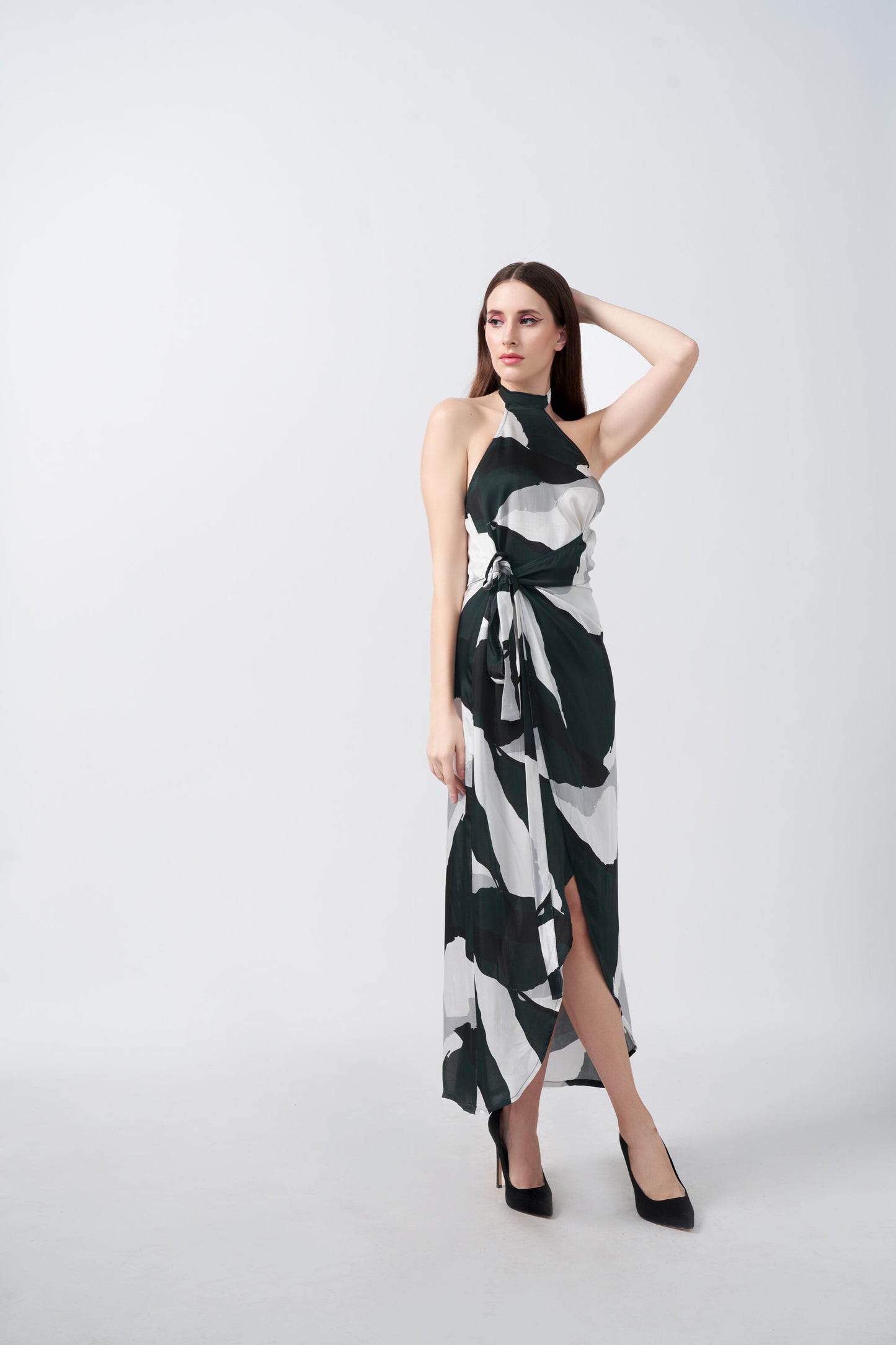 Model posing with one arm raised in a satin dress featuring dark green, black, and white abstract print with asymmetrical hemline.