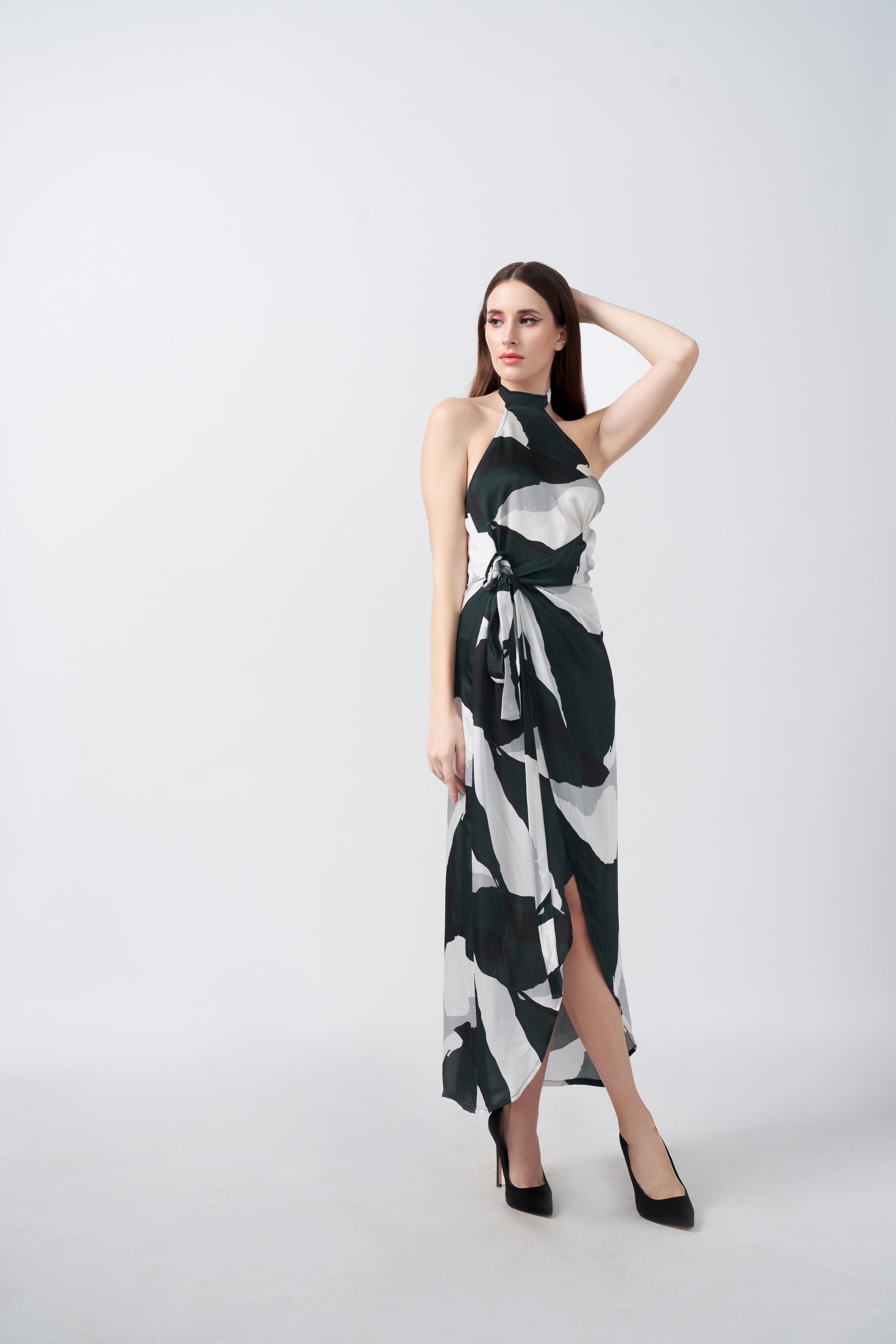 Model posing with one arm raised in a satin dress featuring dark green, black, and white abstract print with asymmetrical hemline.