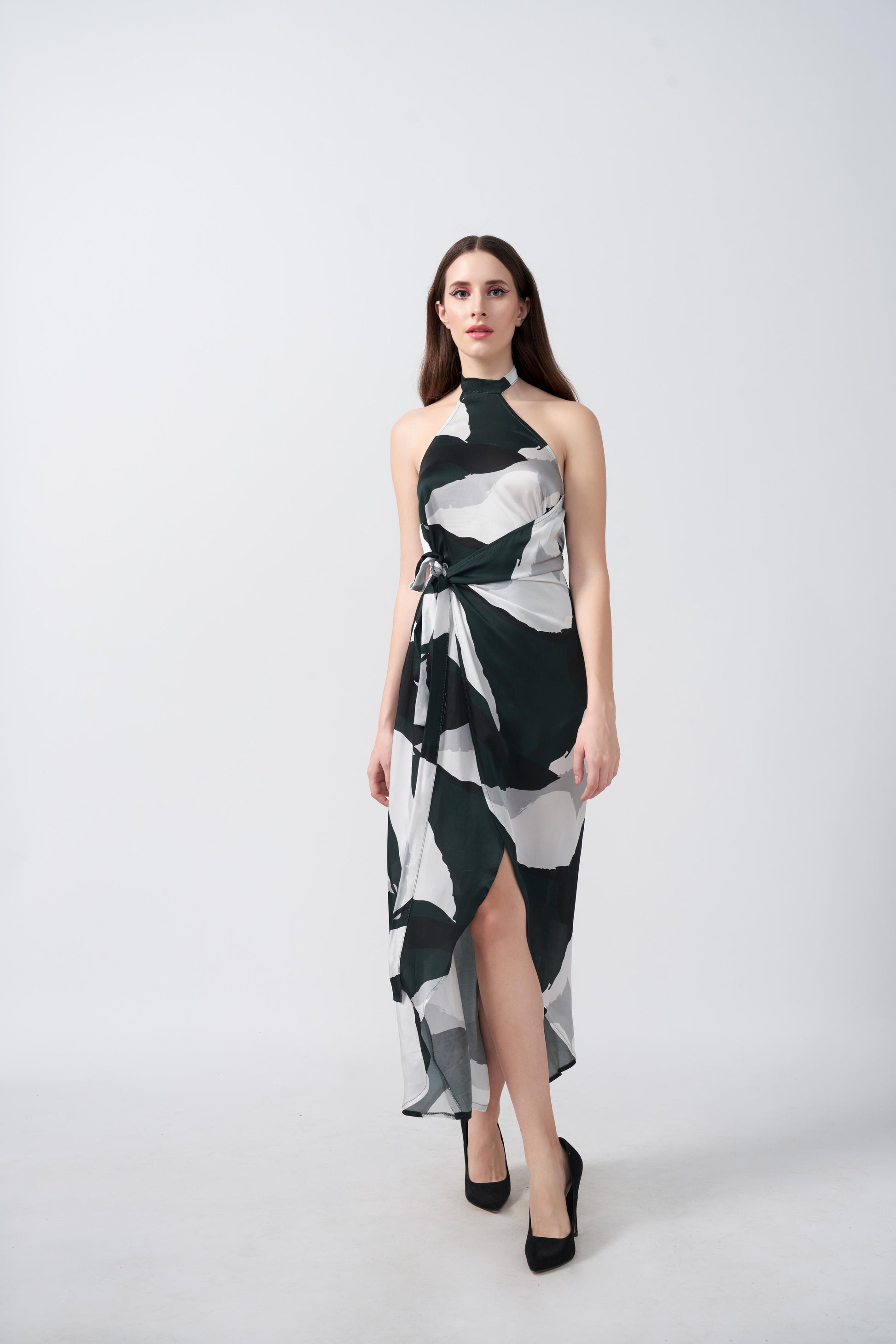 Full-length front view of the model walking in the satin abstract print dress with halter neckline and asymmetrical hem.