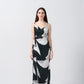 Model standing in a sleeveless ankle-length satin wrap dress with dark green, grey, and black abstract print.