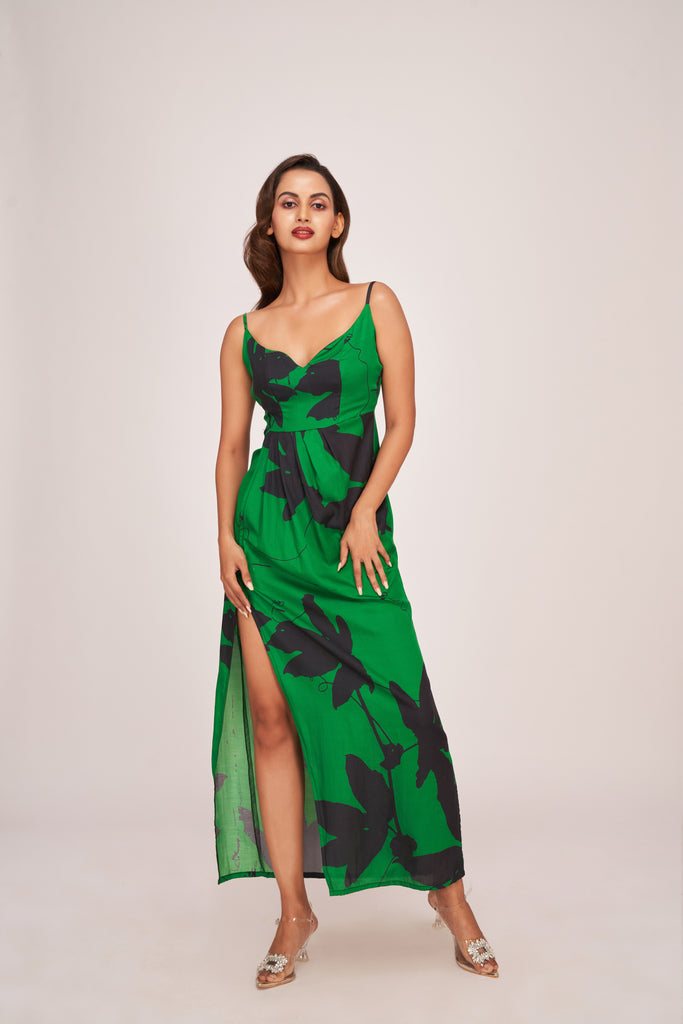 Model in a green satin ankle-length dress with bold black floral print, V-neckline, and thigh-high slit, standing confidently.