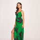 Side-angled pose of model in strap-shoulder green and black satin dress, showing flow and slit detail.