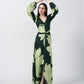 Model standing front-facing with arms raised, wearing a light and dark green floral satin dress with balloon sleeves and a front knot.