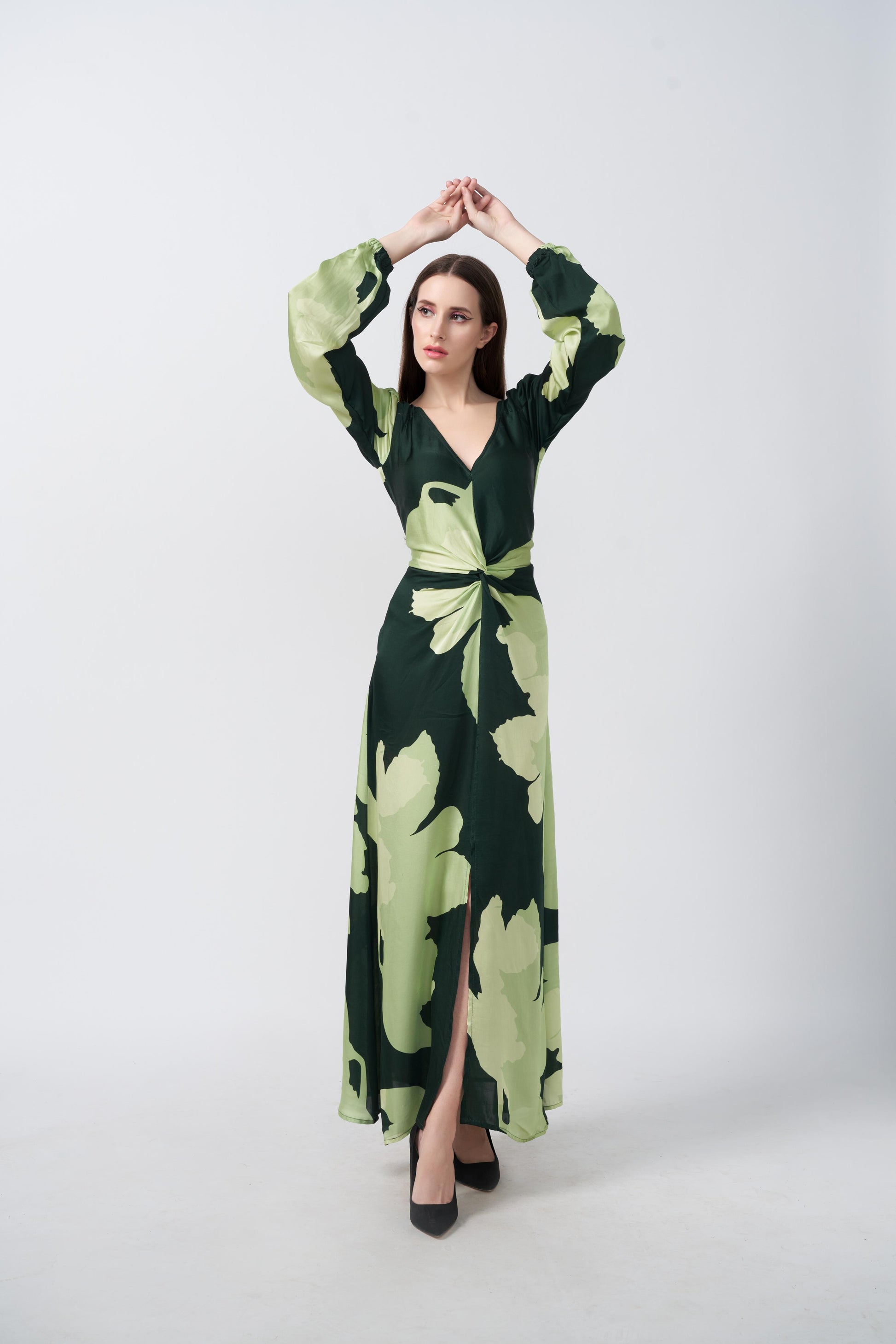 Model standing front-facing with arms raised, wearing a light and dark green floral satin dress with balloon sleeves and a front knot.