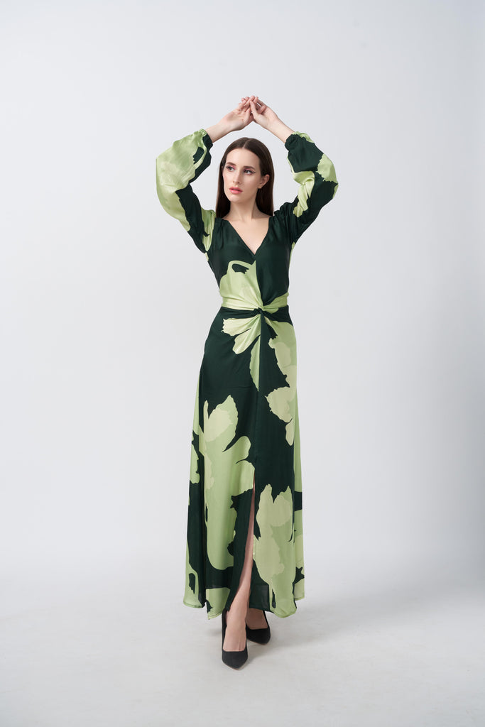 Model standing front-facing with arms raised, wearing a light and dark green floral satin dress with balloon sleeves and a front knot.