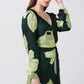 Model in profile pose with hand near face, showcasing the balloon sleeve and elegant V-neckline of the green floral satin dress.