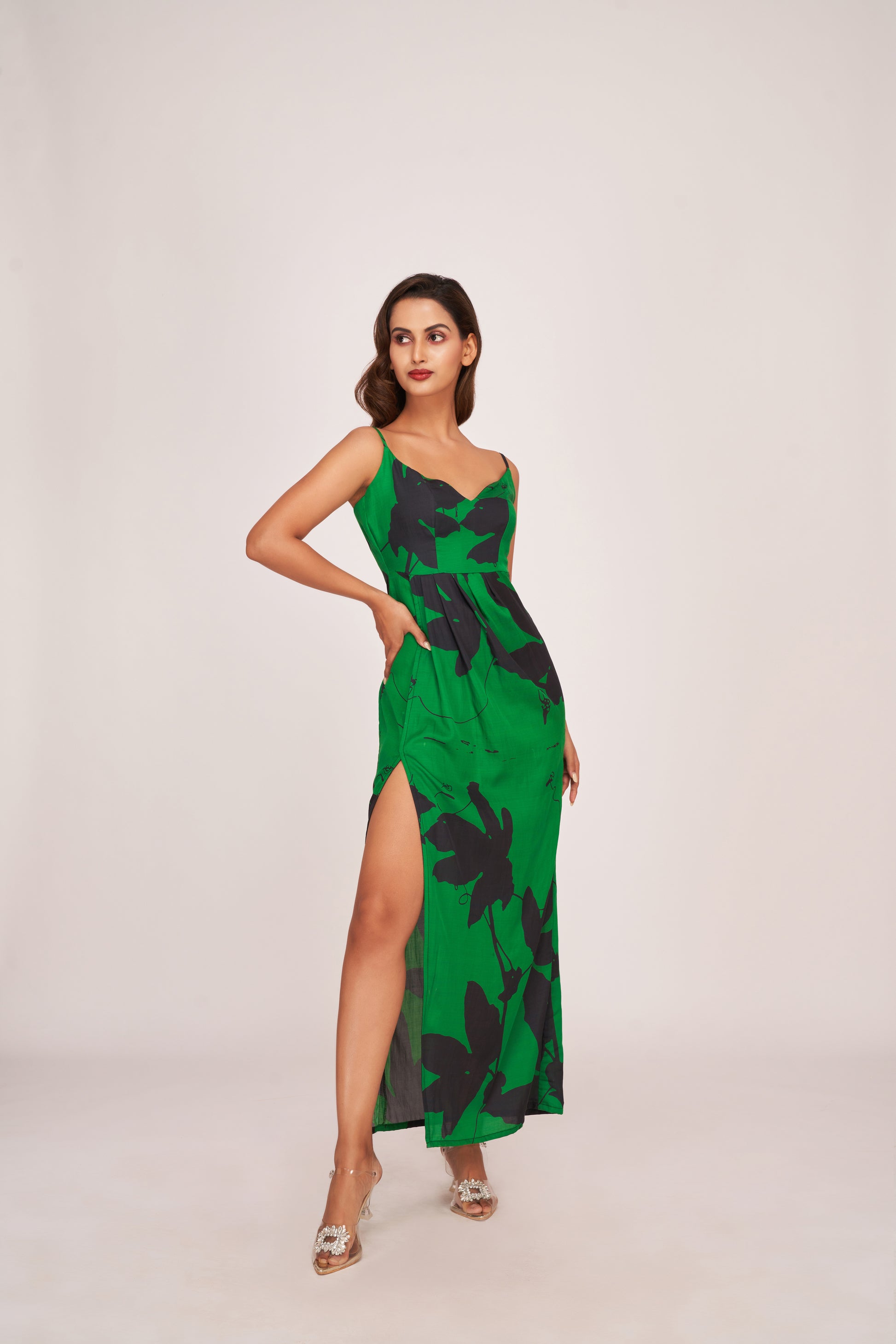 Full-body walking pose of model in green satin dress with bold floral print and high slit in motion.
