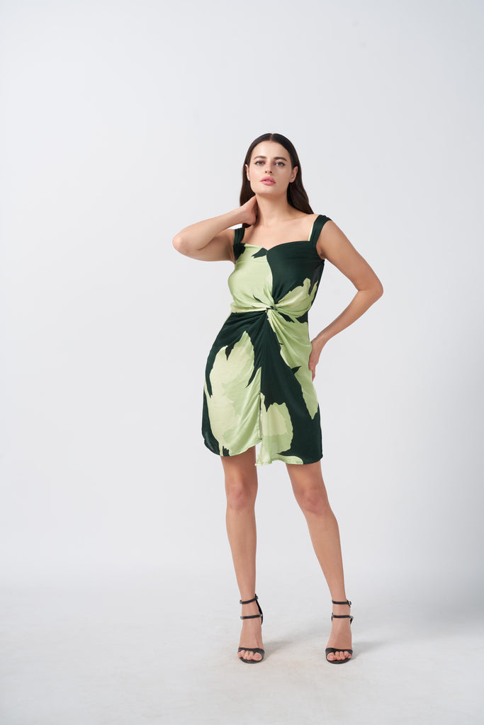 Model posing front-facing in a satin short dress with light and dark green floral print and twisted front knot.
