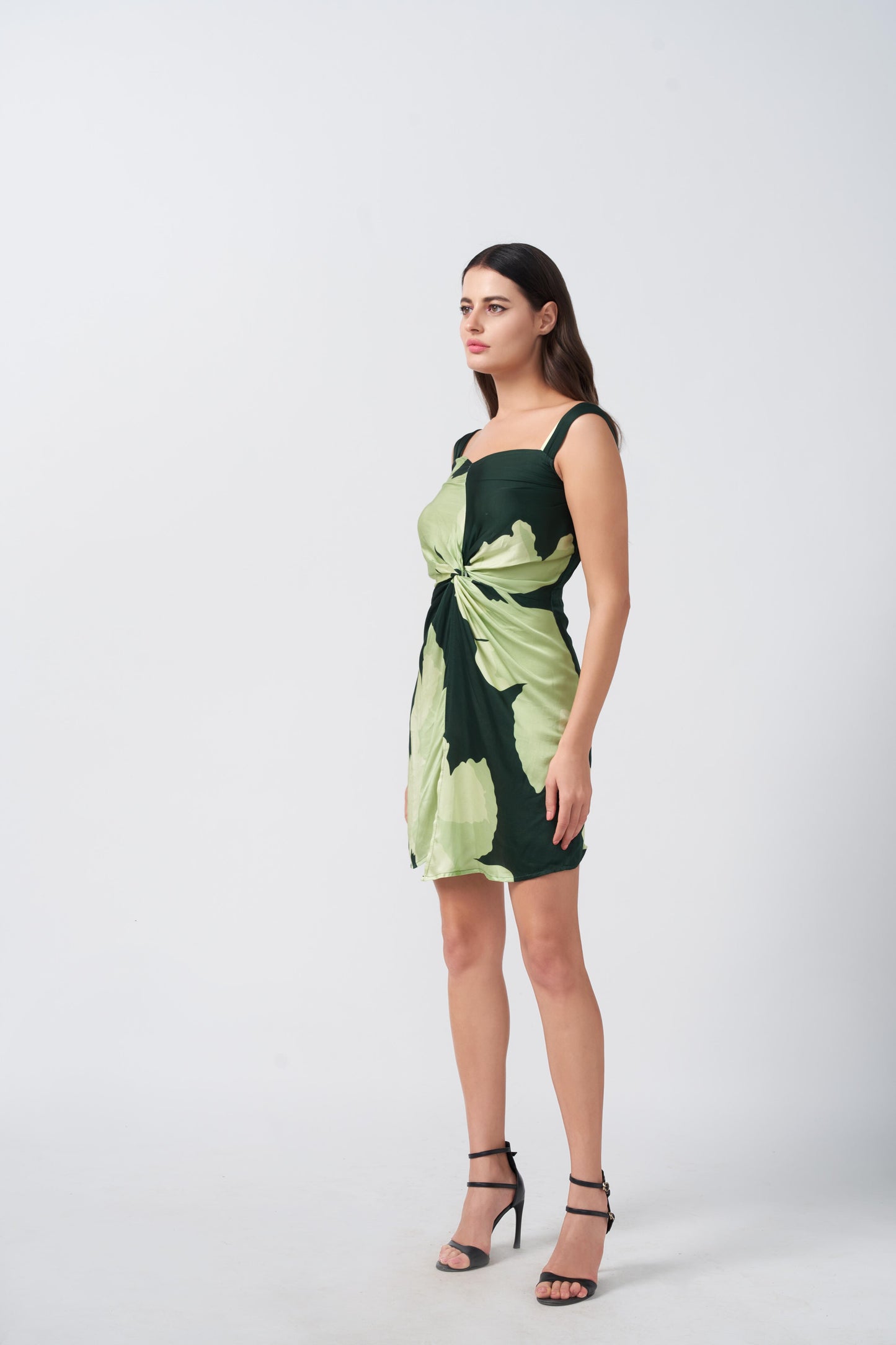 Model in profile view showcasing the elegant shoulder straps and sleek silhouette of the green floral dress.