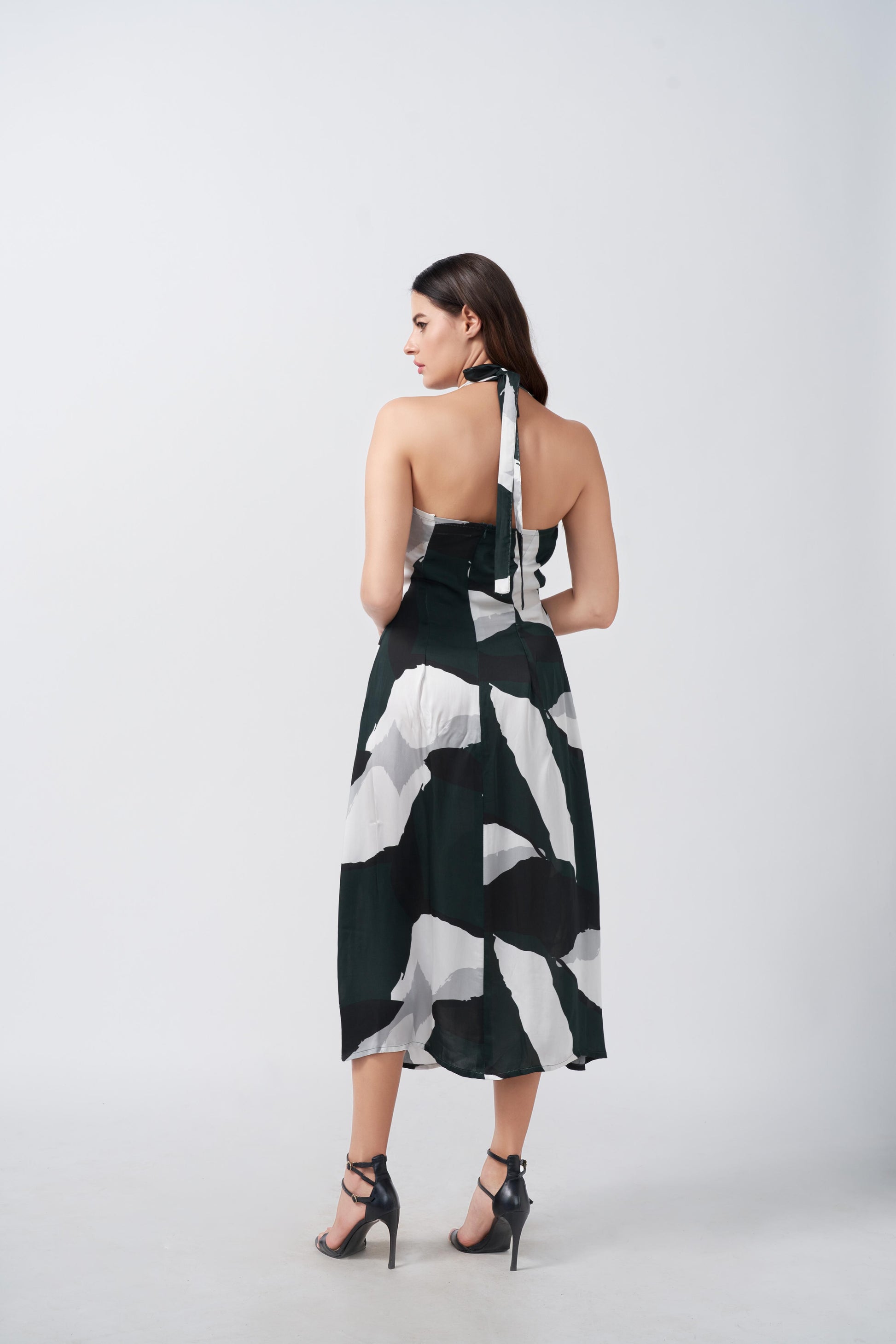 Back view of the model in deep green and white abstract satin dress, showing halter tie-back and asymmetrical hem.