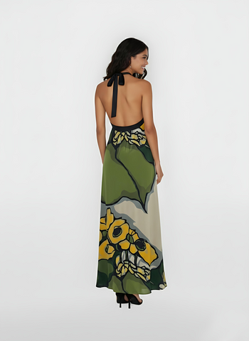 Ankle-length dress showcasing a dramatic backless design with a sleek, black halter tie-neck. The lightweight, airy fabric drapes beautifully from the shoulders, highlighting the bold contrast between the deep green leaves and the soft cream base.