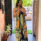 Long halter-neck dress with a vibrant abstract print in shades of olive green, mustard yellow, and black, ideal for summer evening events or resort wear.