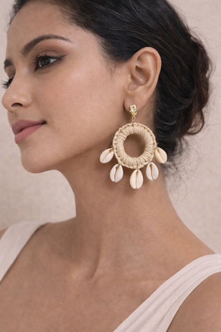 A woman wearing bohemian Shell Ring Drop Earrings featuring five cowrie shells dangling from a woven straw hoop with an imitation gold stud.