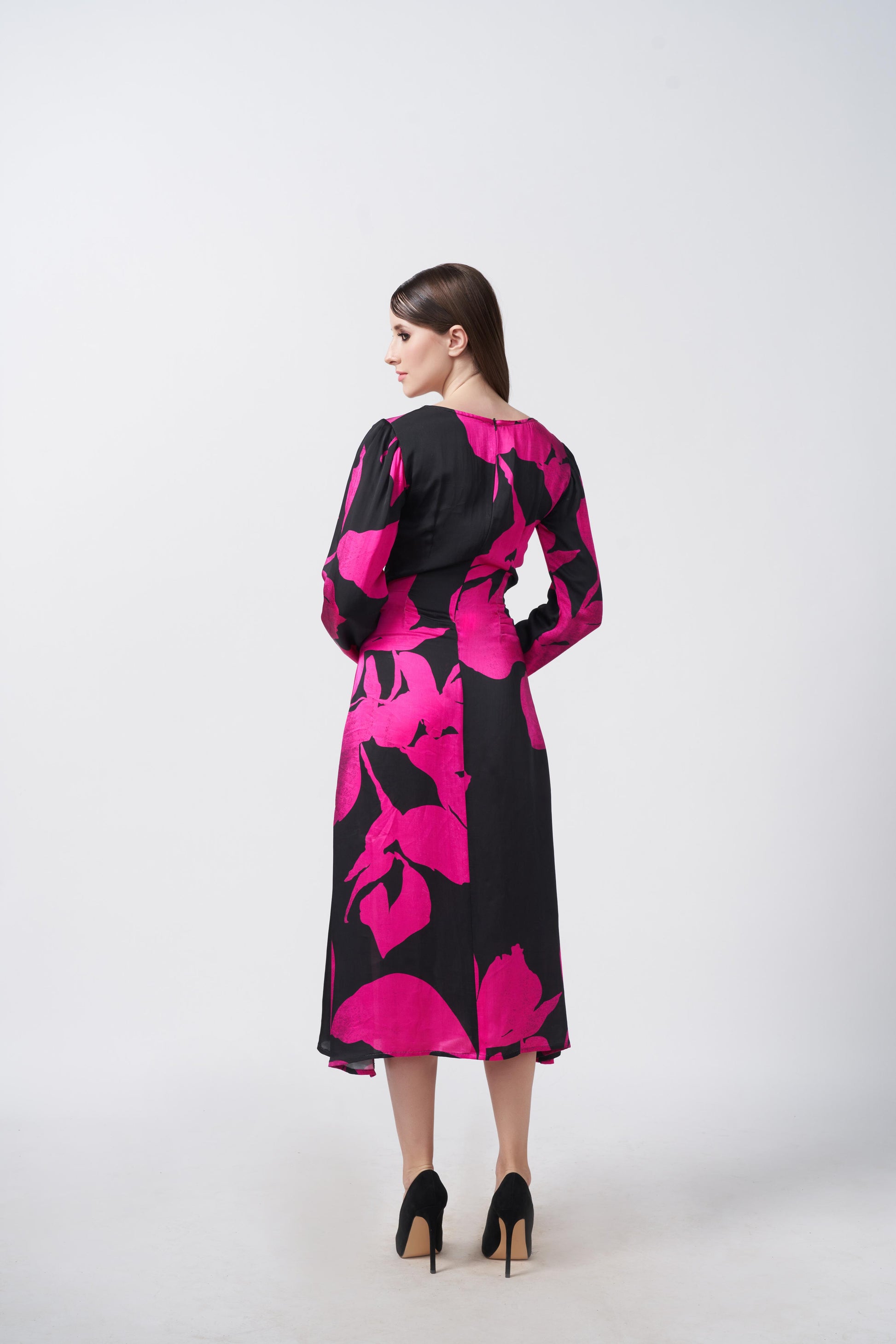 Back view of model highlighting the in pink and black floral midi dress with long sleeves.