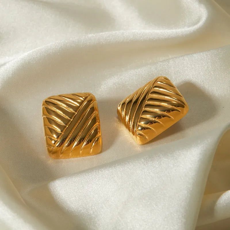A pair of high-shine gold stud earrings featuring a bold, sculpted geometric design with a three-dimensional curved surface
