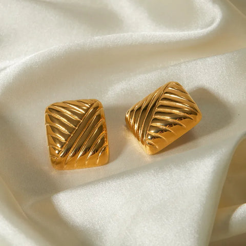 A pair of high-shine gold stud earrings featuring a bold, sculpted geometric design with a three-dimensional curved surface