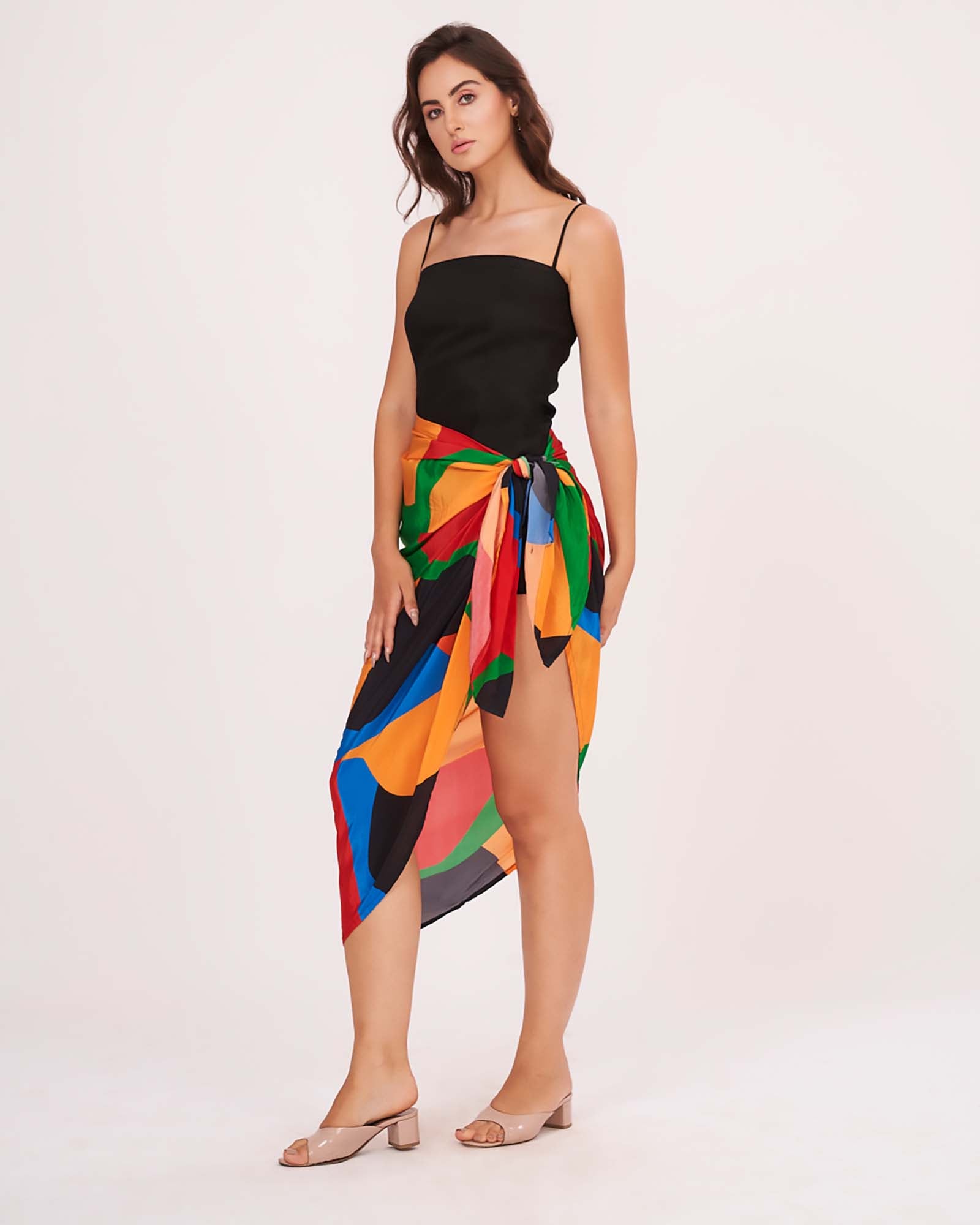 Confident stance with one hand on leg, showing off the abstract print sarong paired with the mini black dress in the co-ord set.