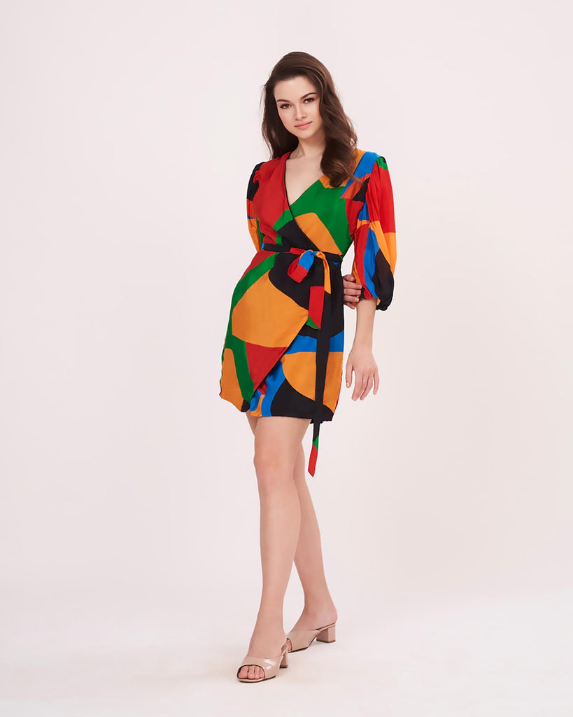 Model wearing a multicolour printed crepe wrap dress with puff sleeves and belt tie-up, standing front-facing with one leg forward.