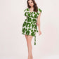 Walking pose of model in green printed knee-length muslin dress with sleeveless cut and flared hem.