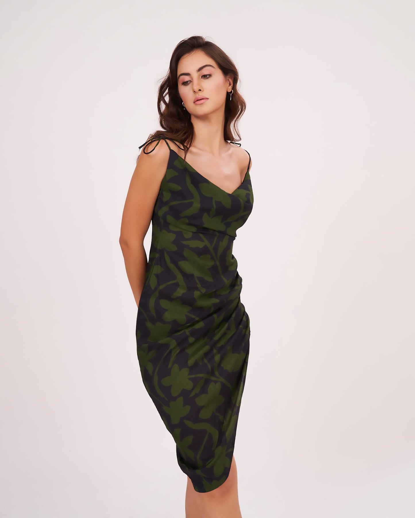 Side-facing pose of model in ruched floral midi dress with asymmetrical hem, showcasing fit and flare.