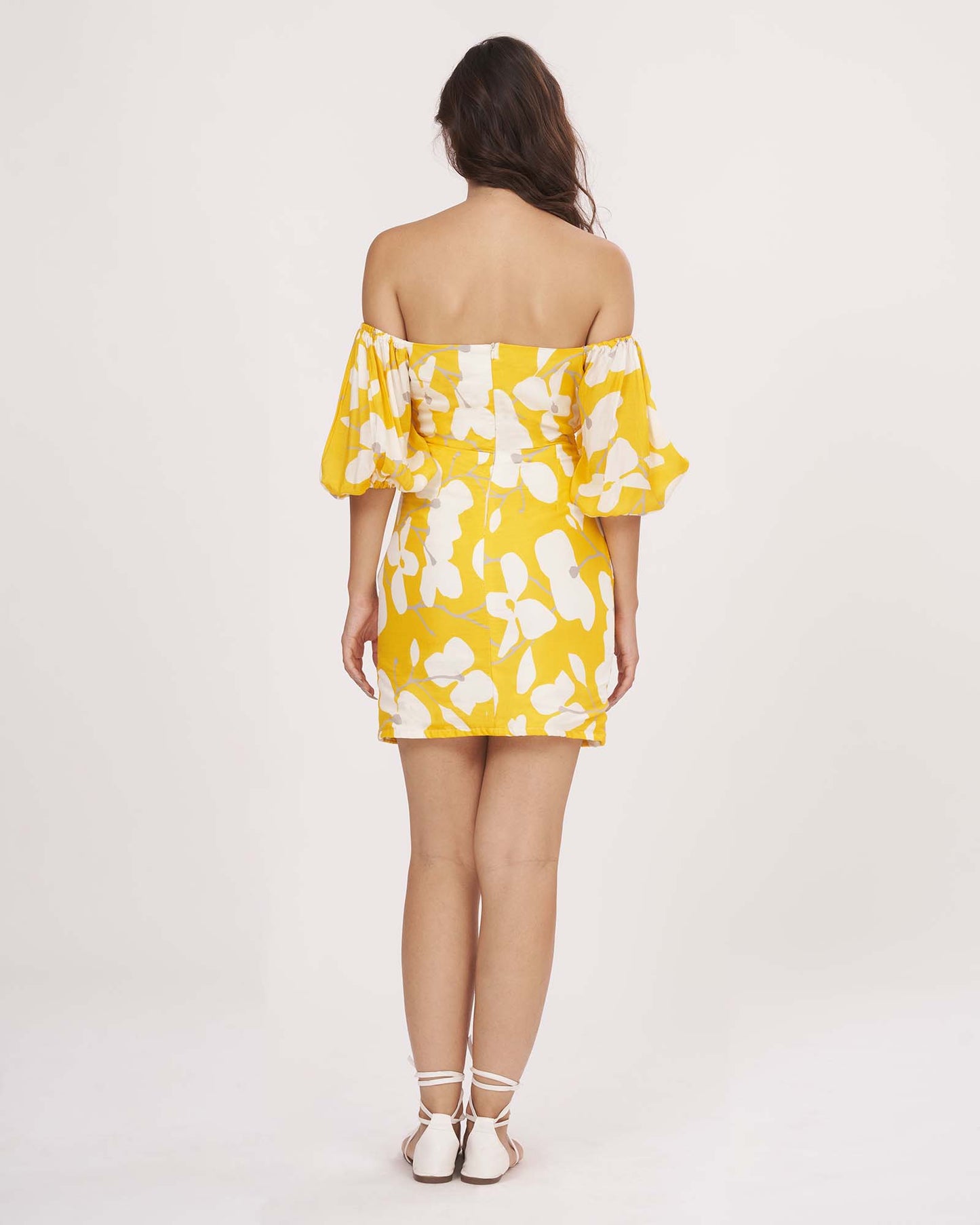 Rear view of the yellow muslin dress showing back zip closure, elasticated puff sleeves, and shoulder cut.