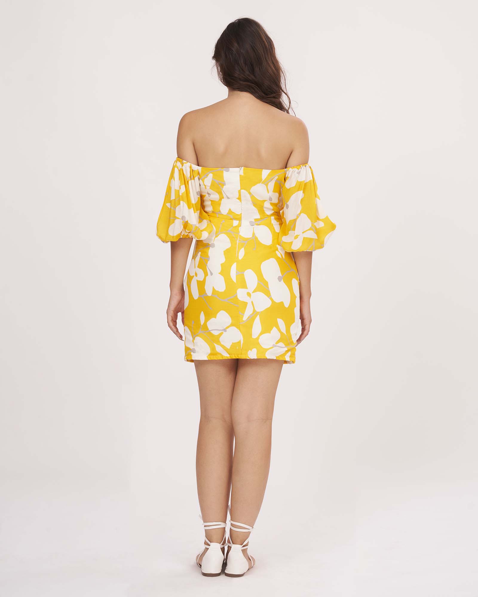 Rear view of the yellow muslin dress showing back zip closure, elasticated puff sleeves, and shoulder cut.