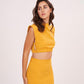 Close-up of the mustard yellow co-ord set showing the boat neckline and fitted bodice, emphasizing the sleek tailoring and structured form.