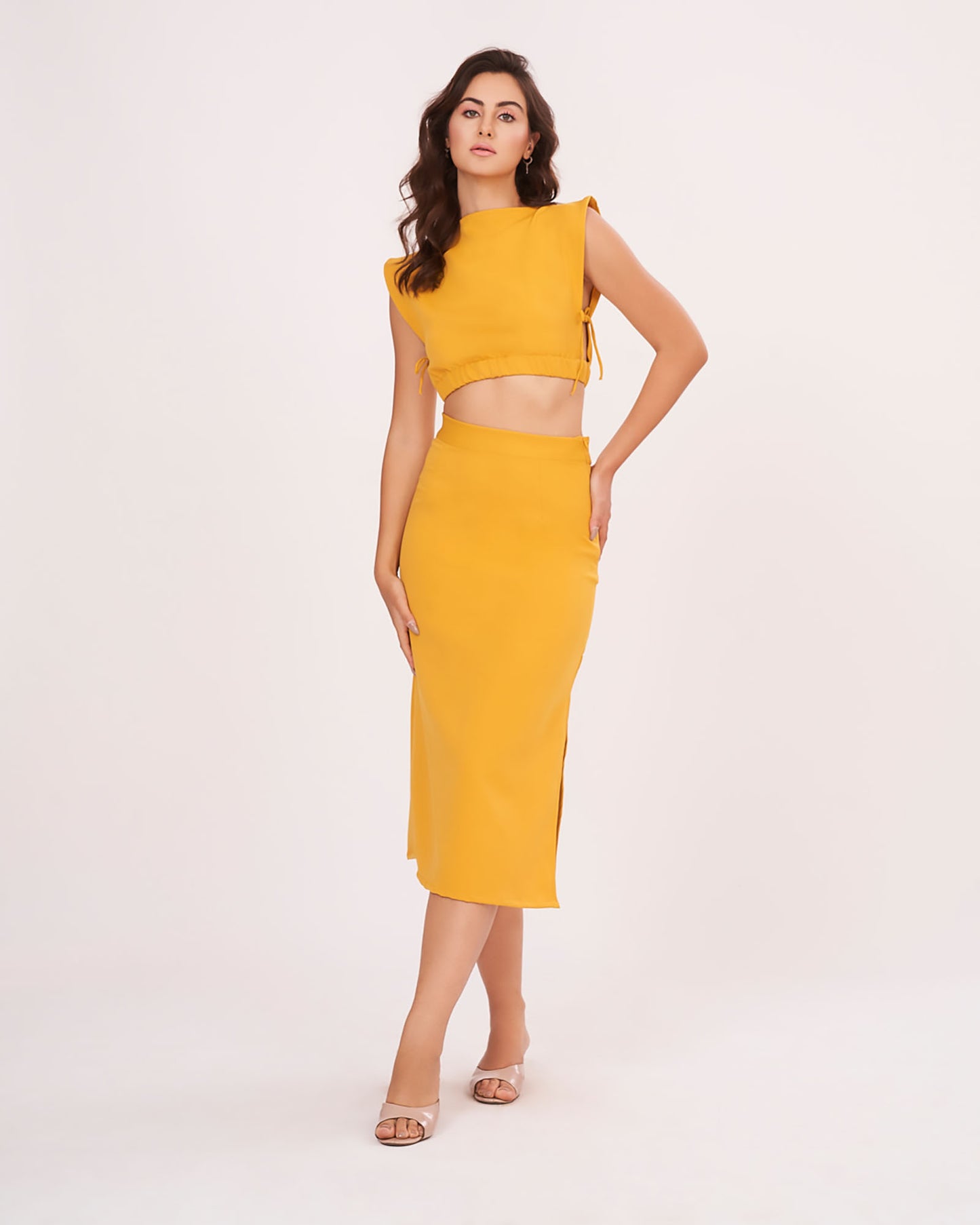 Model poses in a mustard yellow co-ord set with a boat neck sleeveless blouse and a long straight skirt