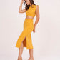 Model poses with one hand resting on her head and one leg slightly lifted, revealing the side slit of the mustard yellow skirt for a bold, modern flair.