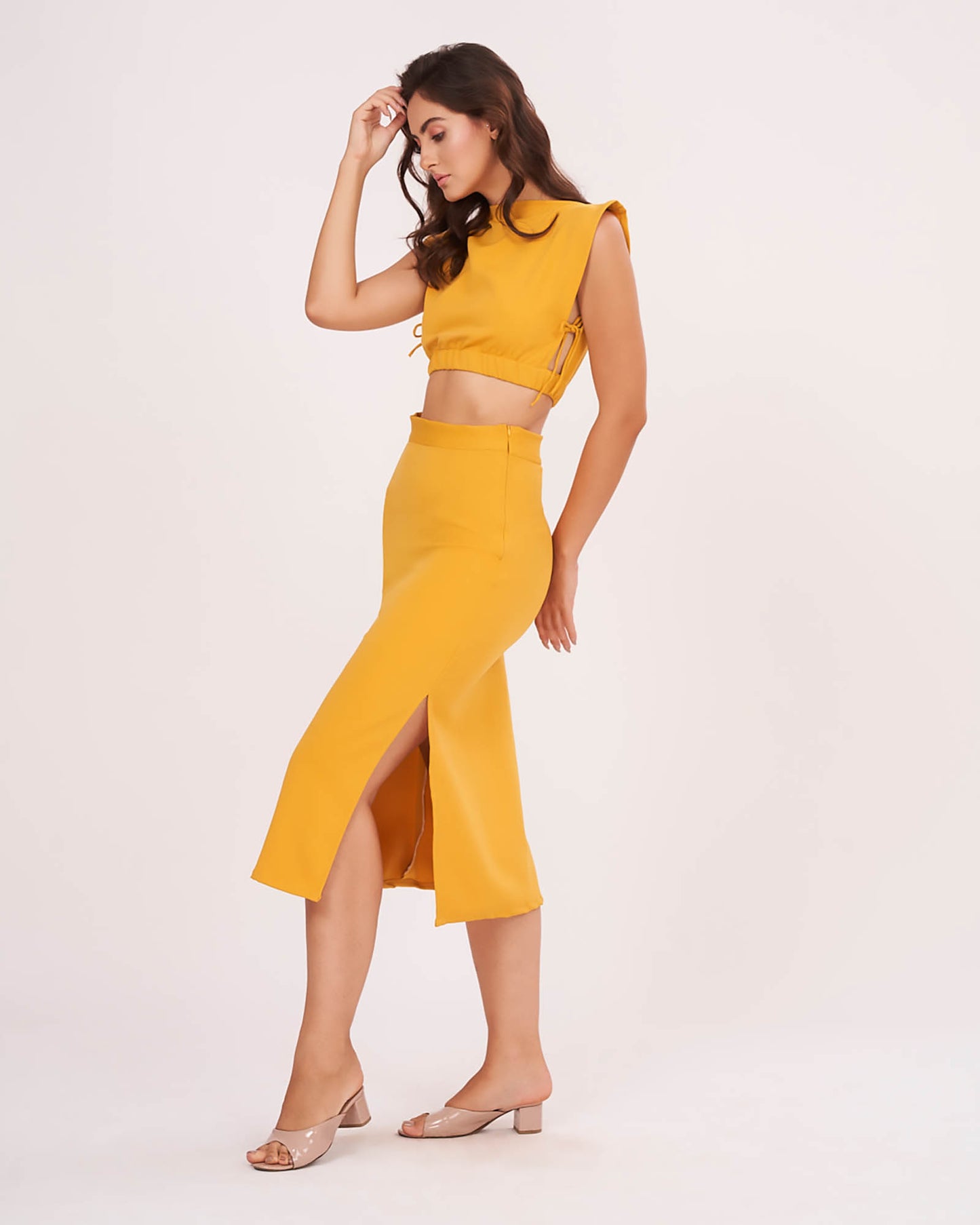 Model poses with one hand resting on her head and one leg slightly lifted, revealing the side slit of the mustard yellow skirt for a bold, modern flair.