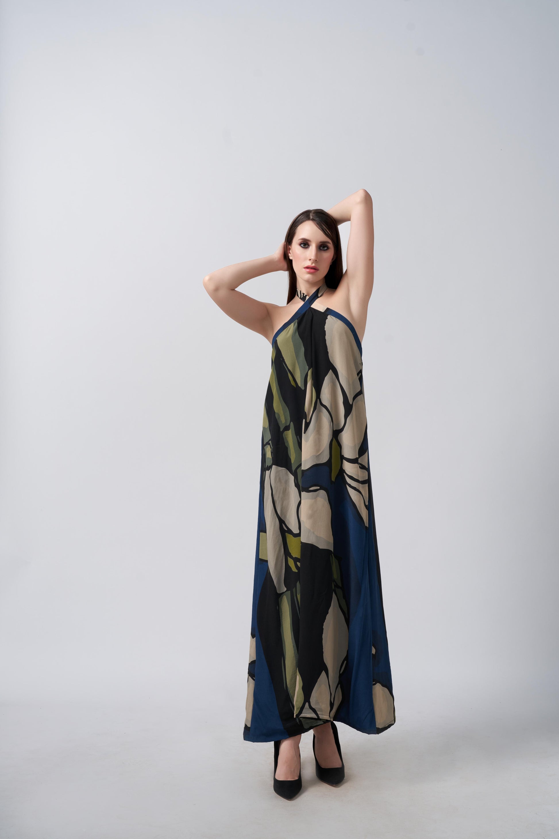 Model posing front-facing in navy blue and beige abstract floral halter neck dress, arms raised to showcase neckline.