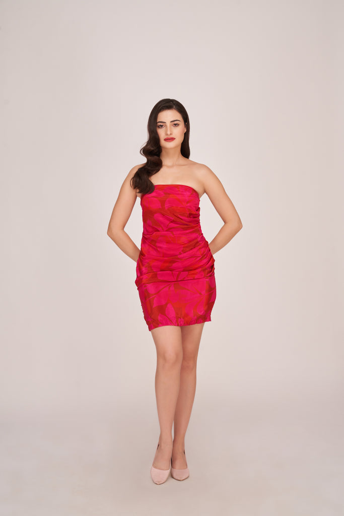 Model in a pink off-shoulder mini dress with floral print and ruched front, standing confidently with hands on hips