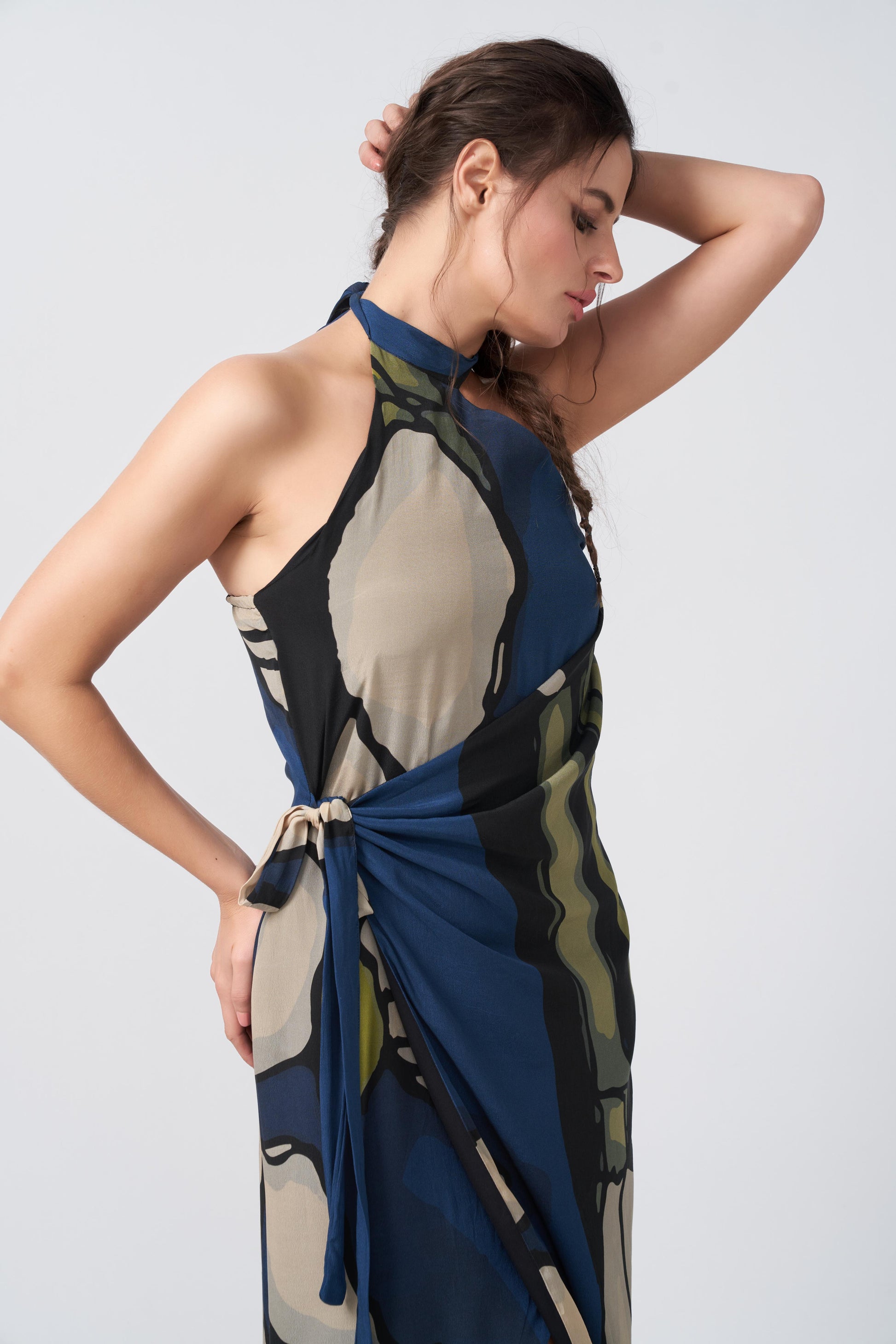 Close-up side angle of model wearing navy blue crepe dress with halter neck and asymmetric shoulder cut.