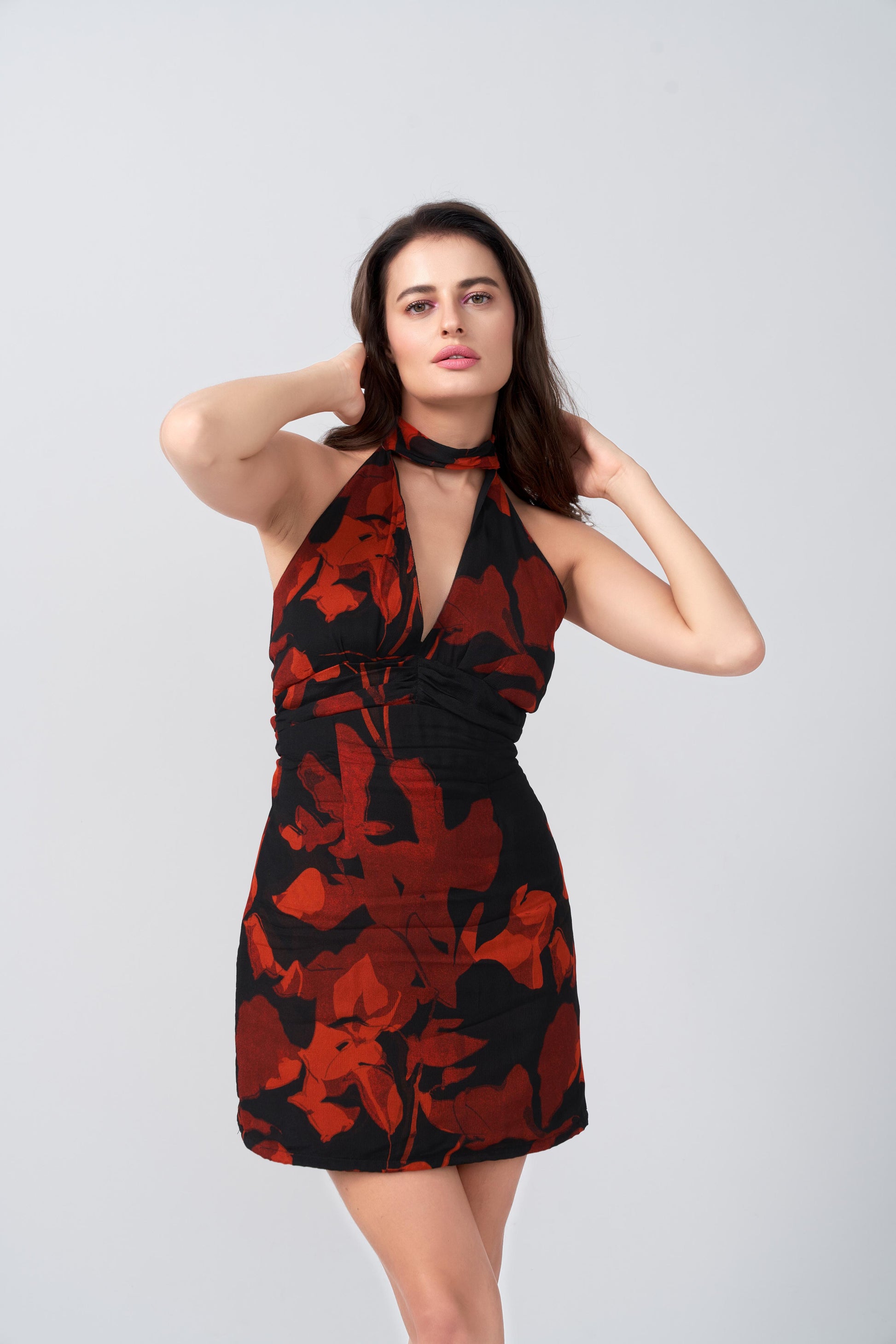Model posing with hand near face in orange and black floral print dress, drawing attention to neckline and print.