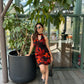 Model seated outdoors in orange and black printed short dress, highlighting relaxed and playful elegance.