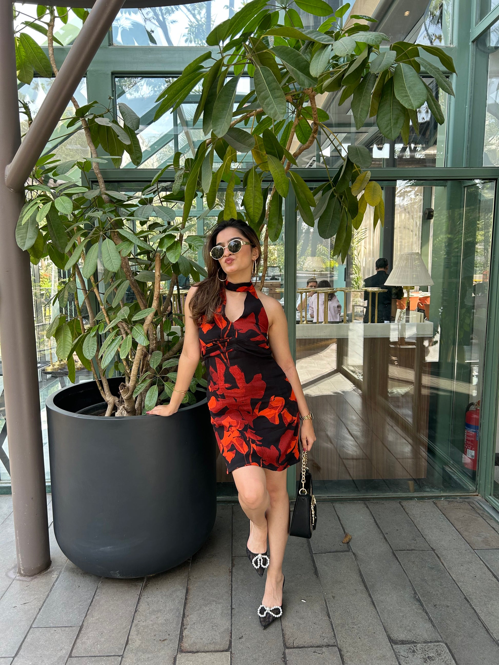 Model seated outdoors in orange and black printed short dress, highlighting relaxed and playful elegance.