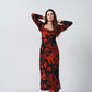 Front view of model wearing an orange and black ankle-length dress with overlapped neck and long sleeves.