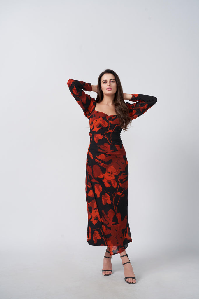 Front view of model wearing an orange and black ankle-length dress with overlapped neck and long sleeves.